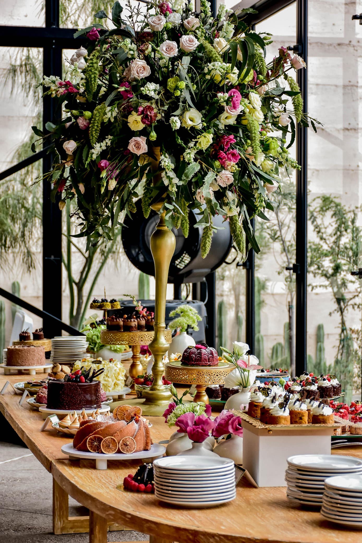 Mesa de postres con repostería individual y arreglo de flores para un evento